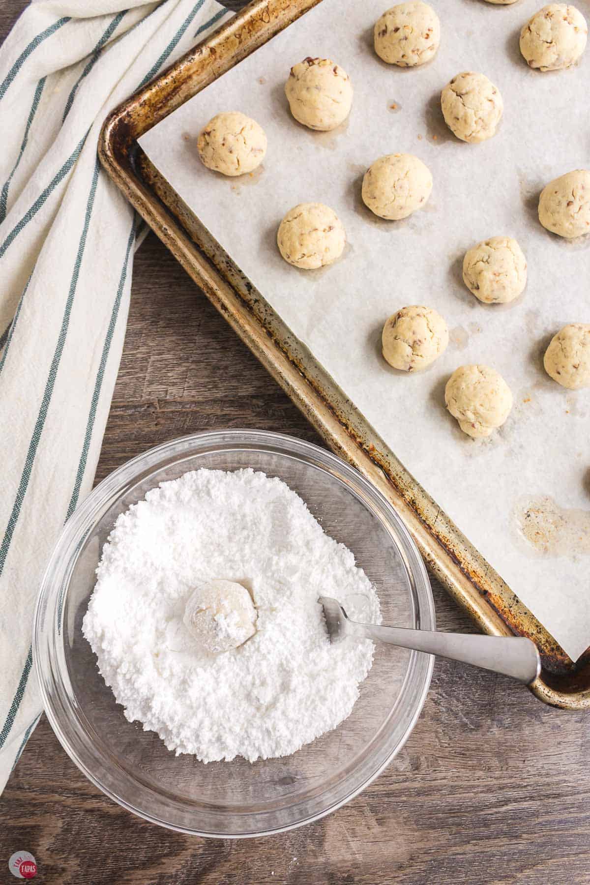 cookie being rolled in a bowl of powdered sugar
