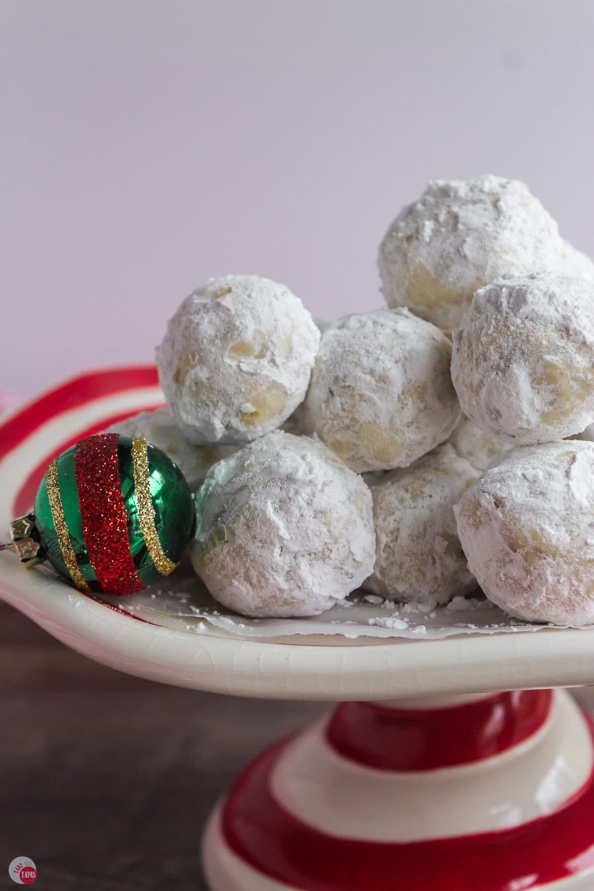 red and white cake plate with a stack of snowball cookies on top
