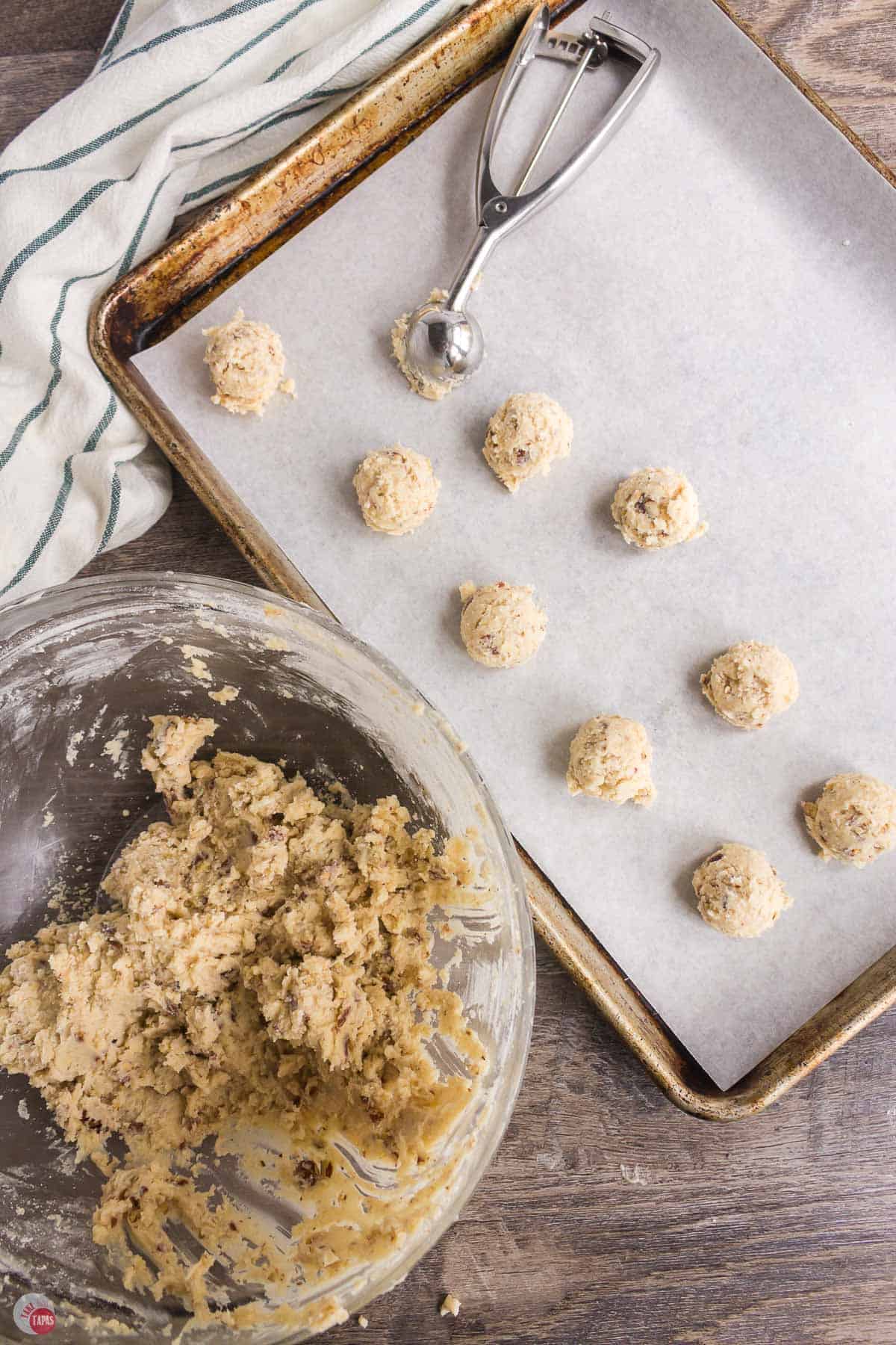 bowl of cookie dough being scooped onto a baking sheet with parchment paper