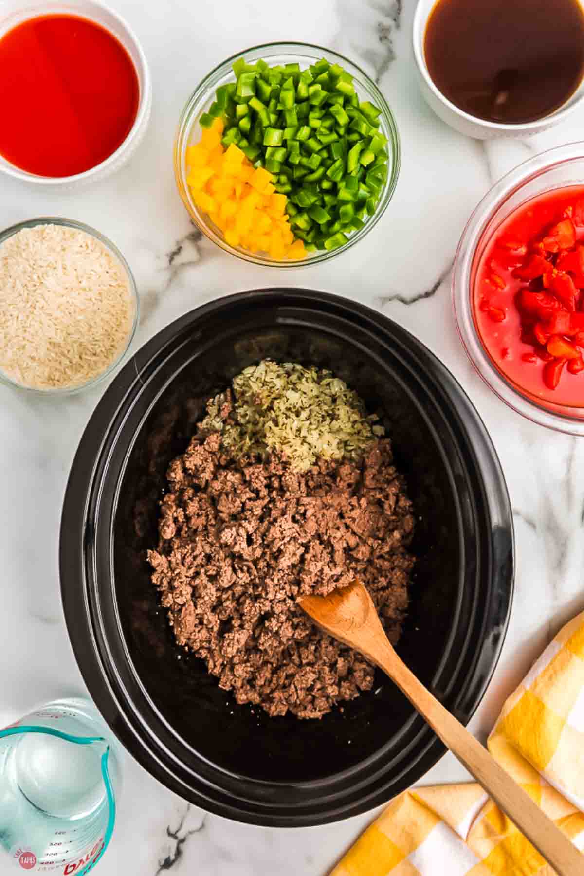 cooked ground beef and onions in slow cooker with a wood spoon
