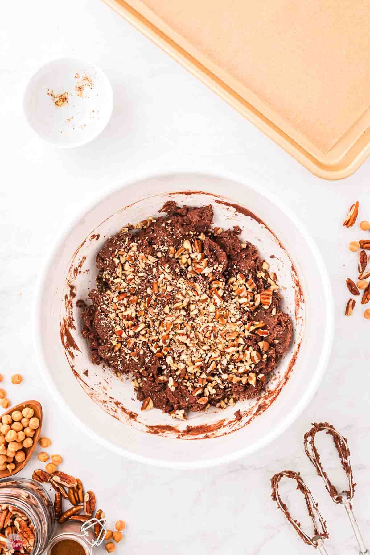 chocolate cookie dough in a white bowl with chopped pecans on top