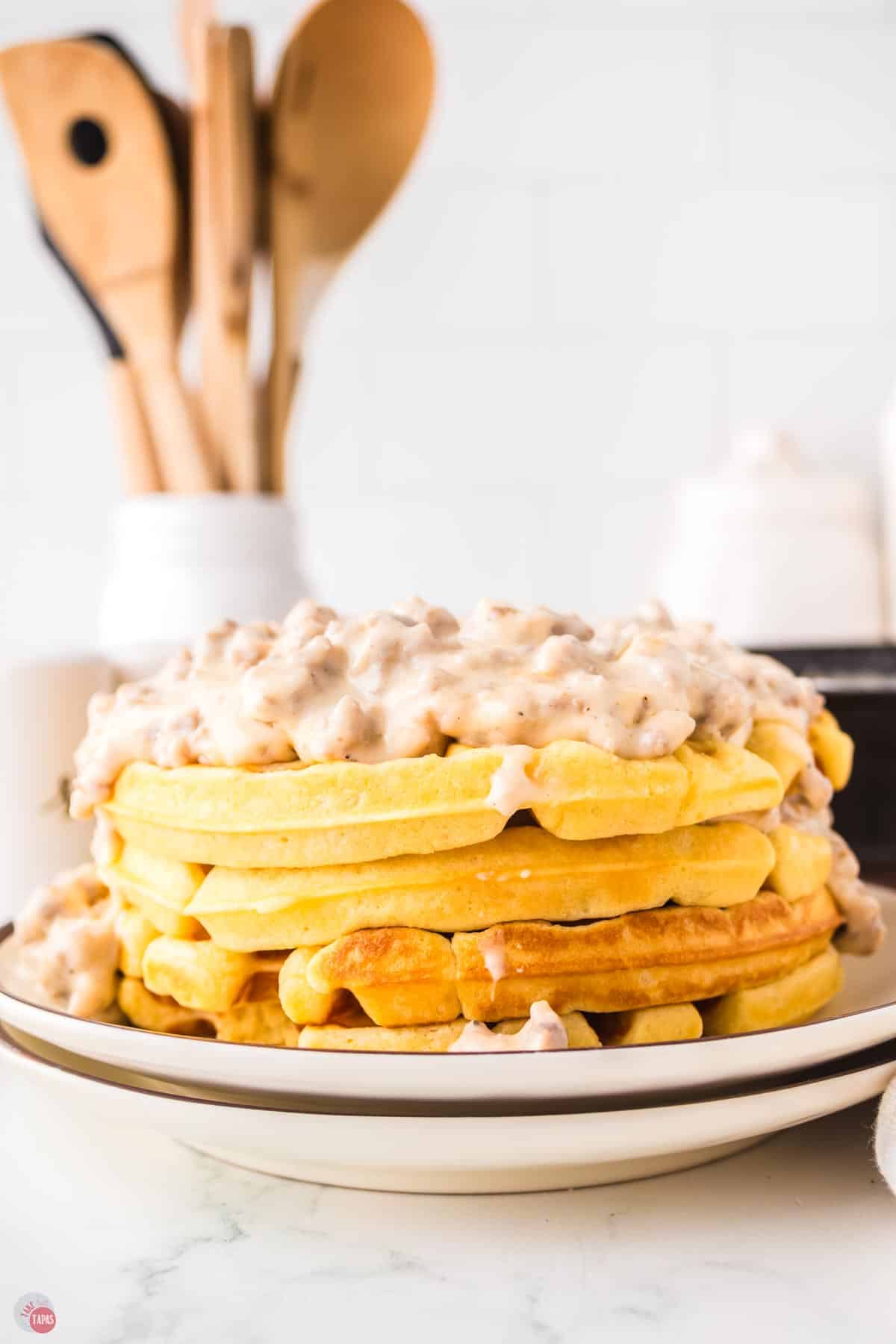 stack of 4 waffles topped with sausage gravy on two white plates