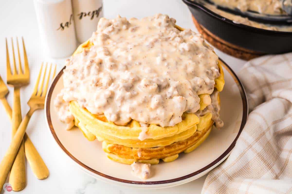 pork sausage gravy on top of a waffle on stack of plates
