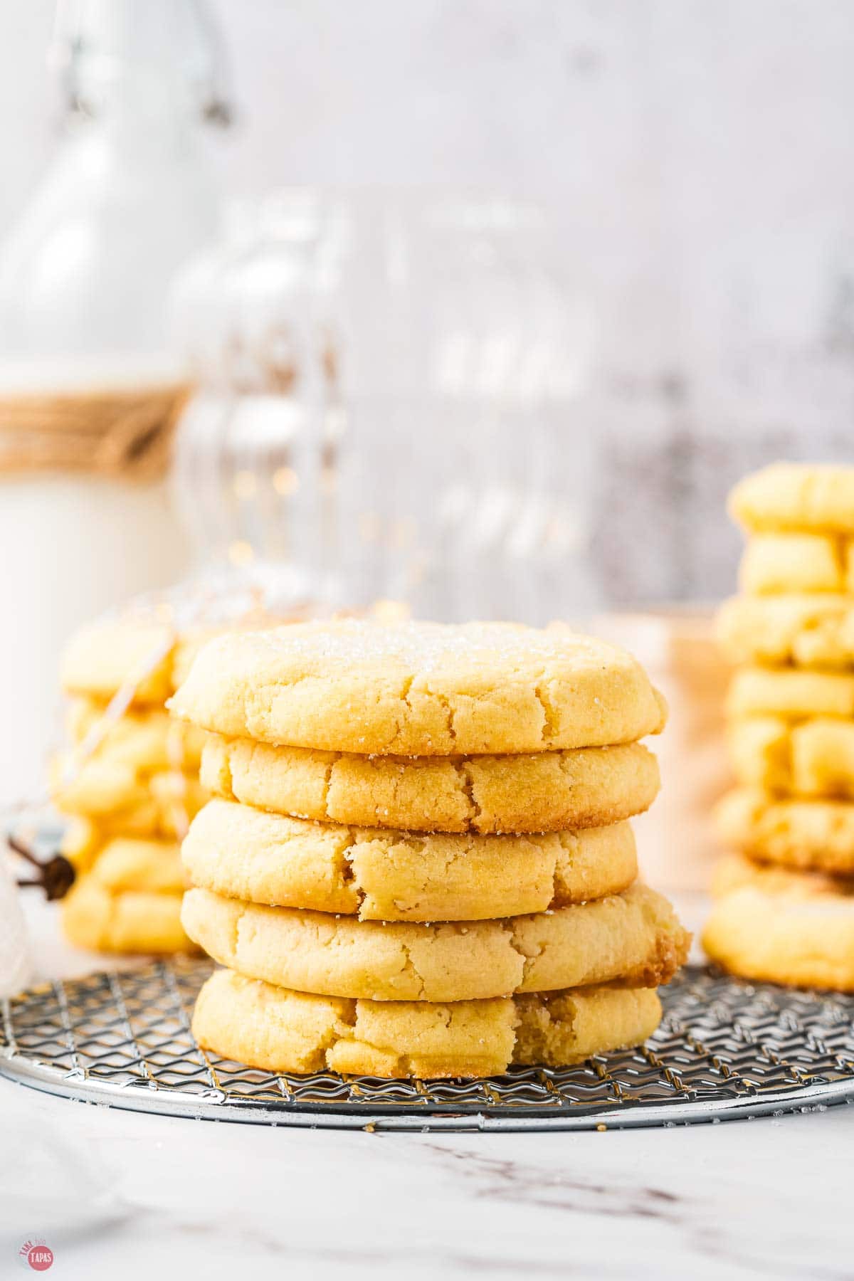 stack of sugar cookies on a cooling rack with a glass of milk