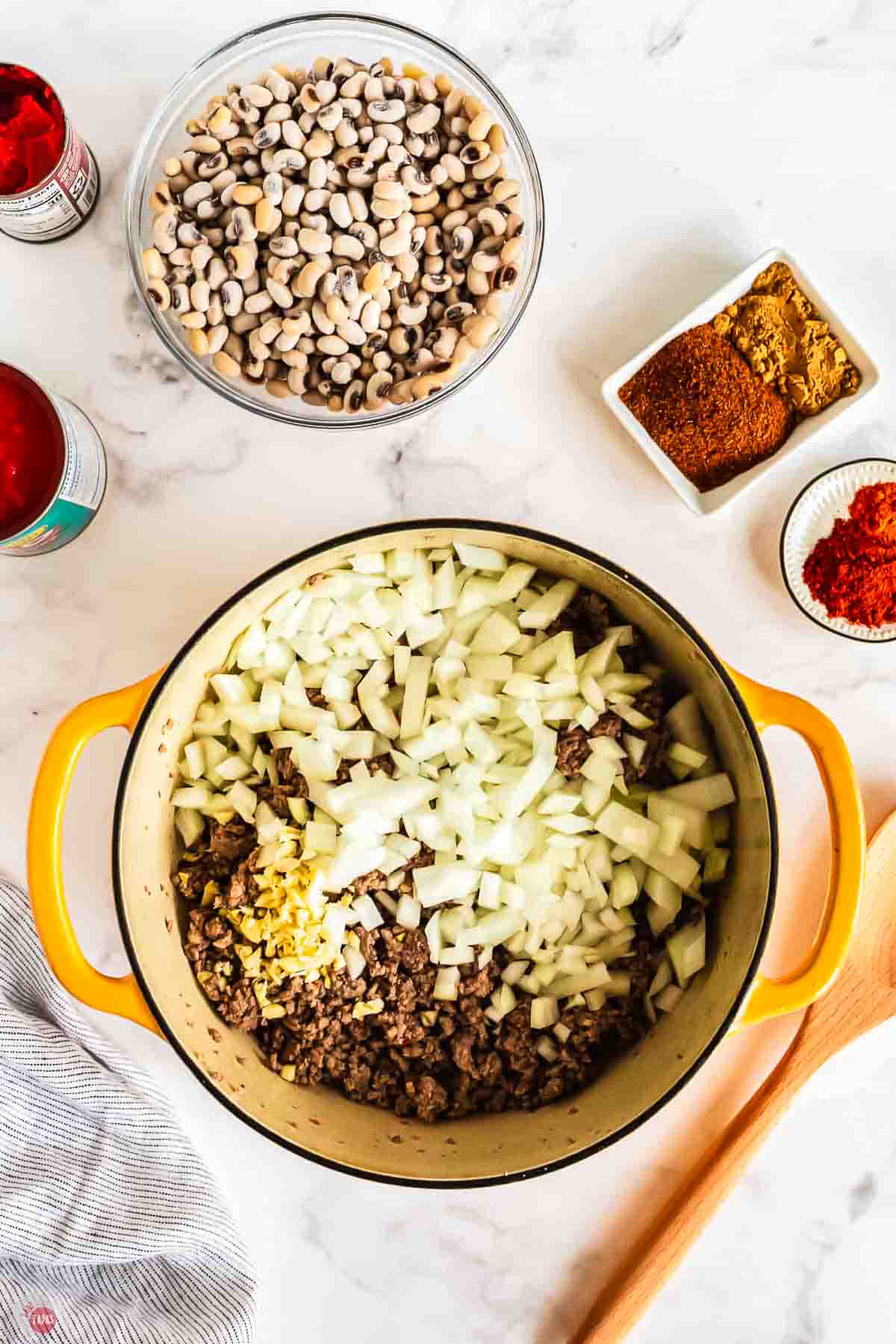chopped onion and garlic on top of ground beef in a yellow pot