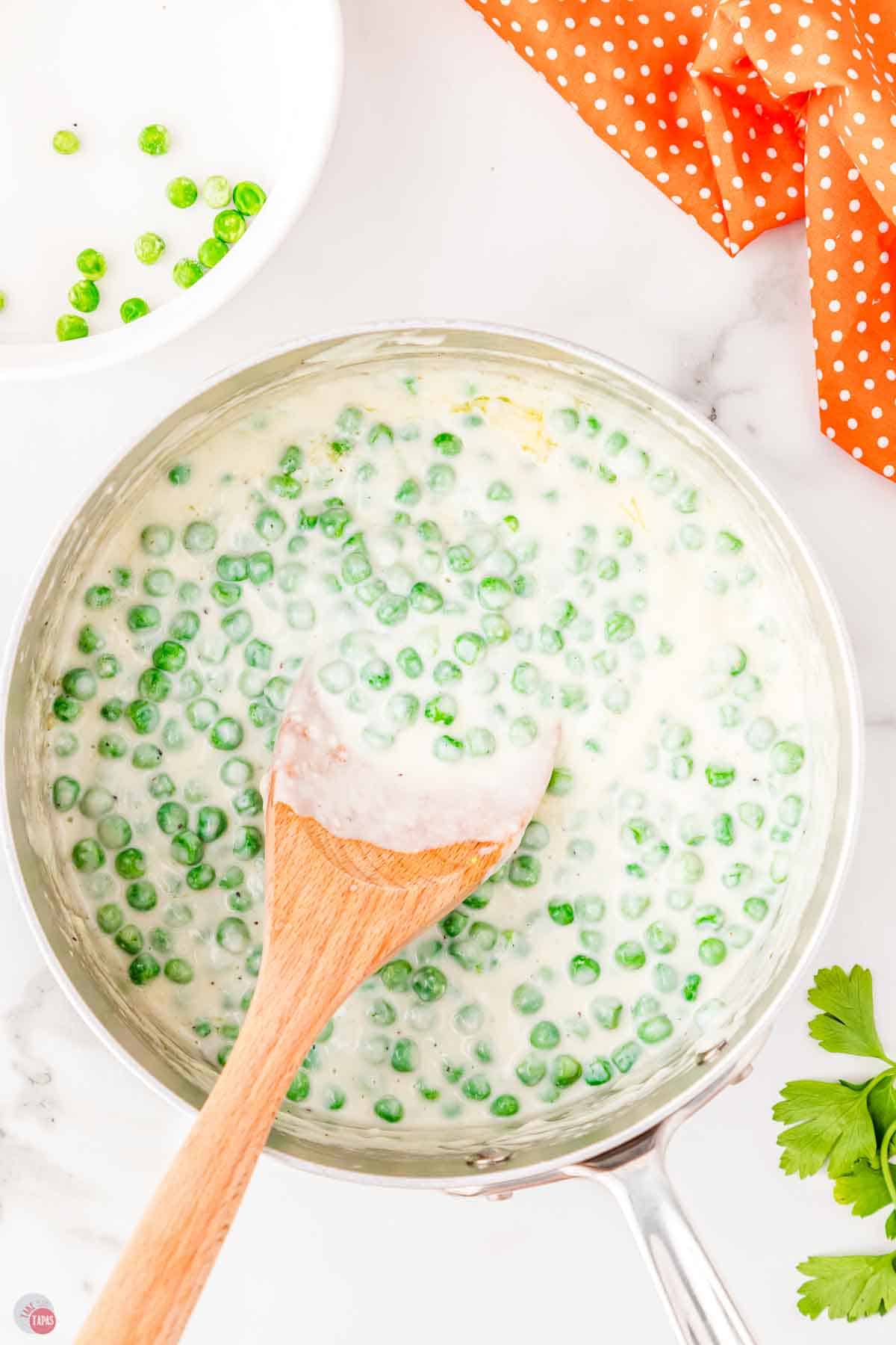 skillet of creamed peas with a wood spoon