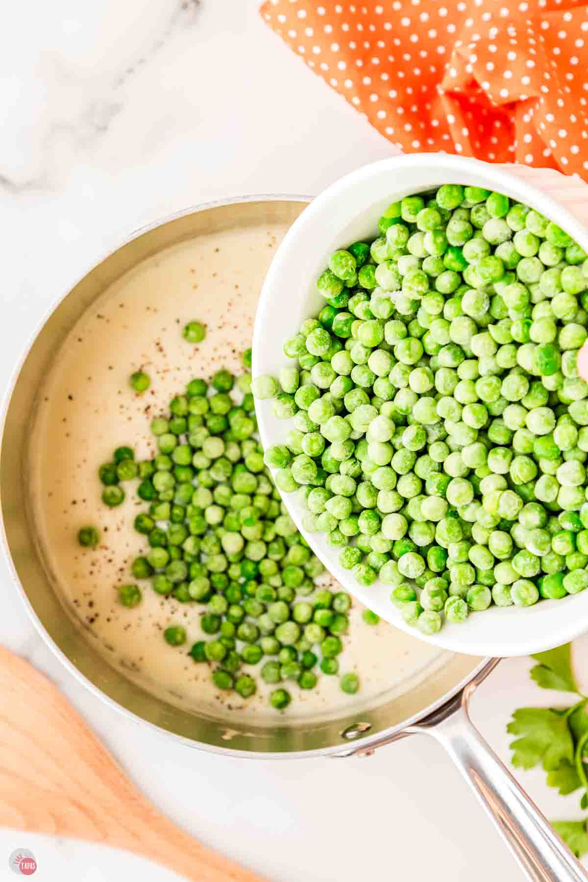 frozen peas pouring into a skillet with cream sauce