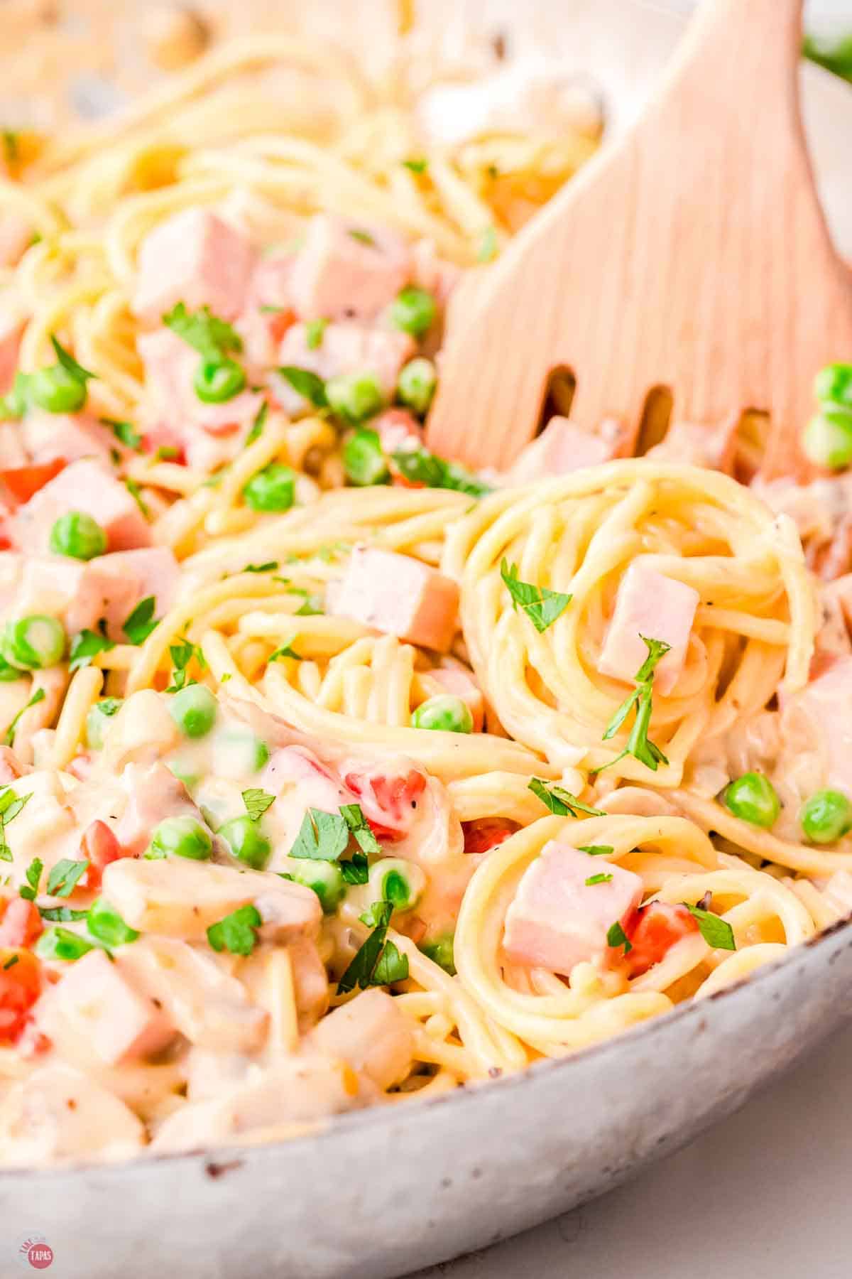 close up of pasta with peas and ham with a wood spoon
