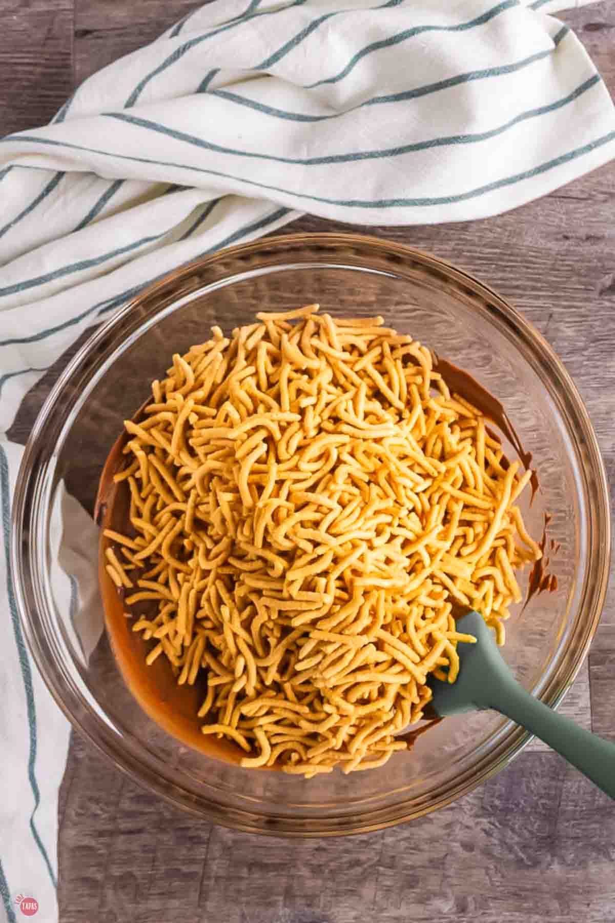 bowl of chow mein noodles next to a napkin with a grey spatula