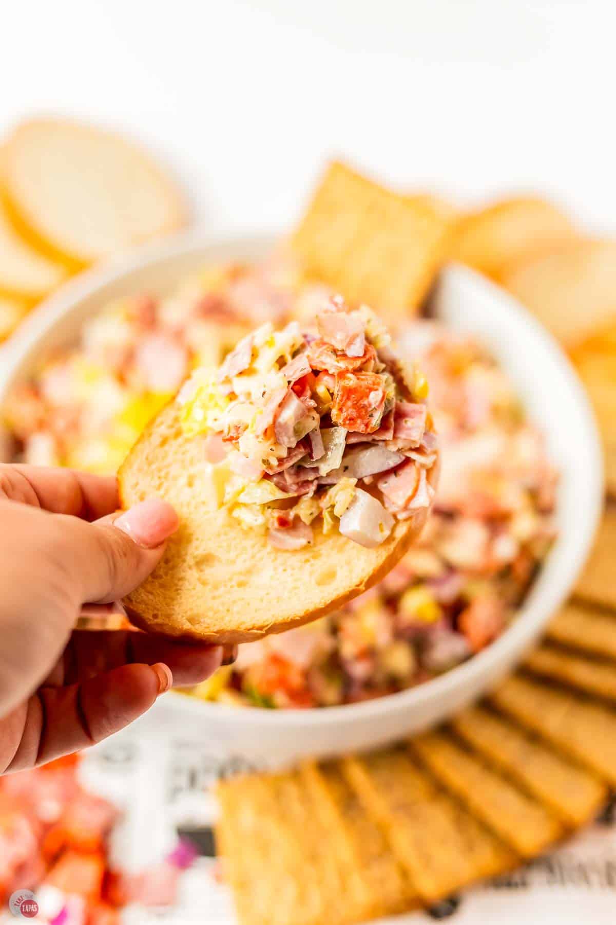hand with crostini with scoop of hoagie dip on it
