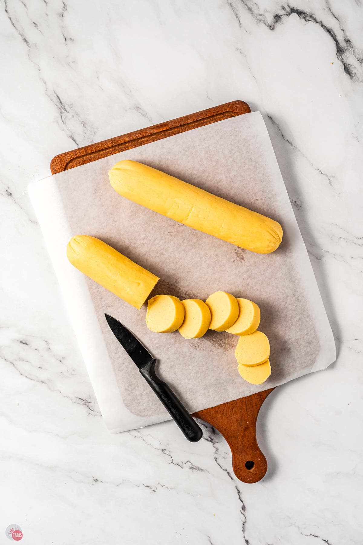 cookie dough logs being cut into slices on a pieces of parchment paper