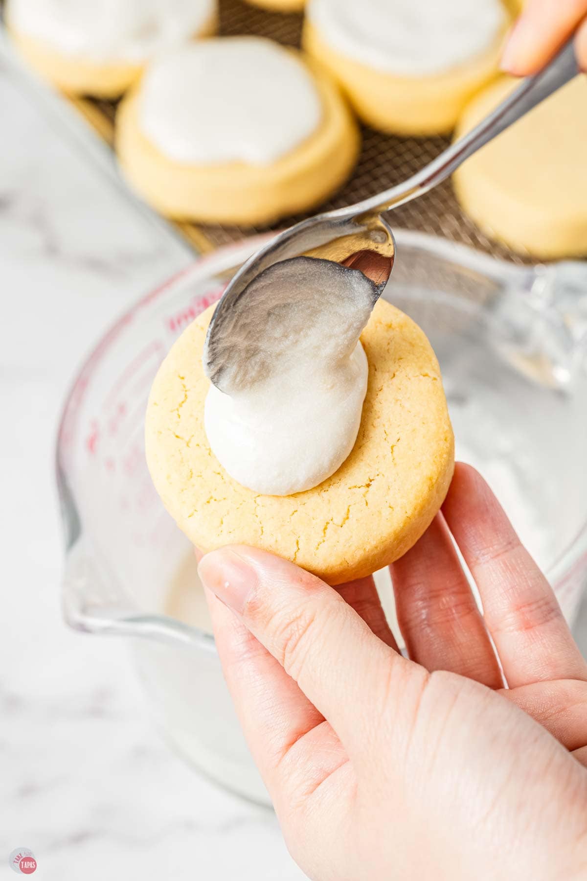 hand holding a cookie with a spoon drizzling icing on top