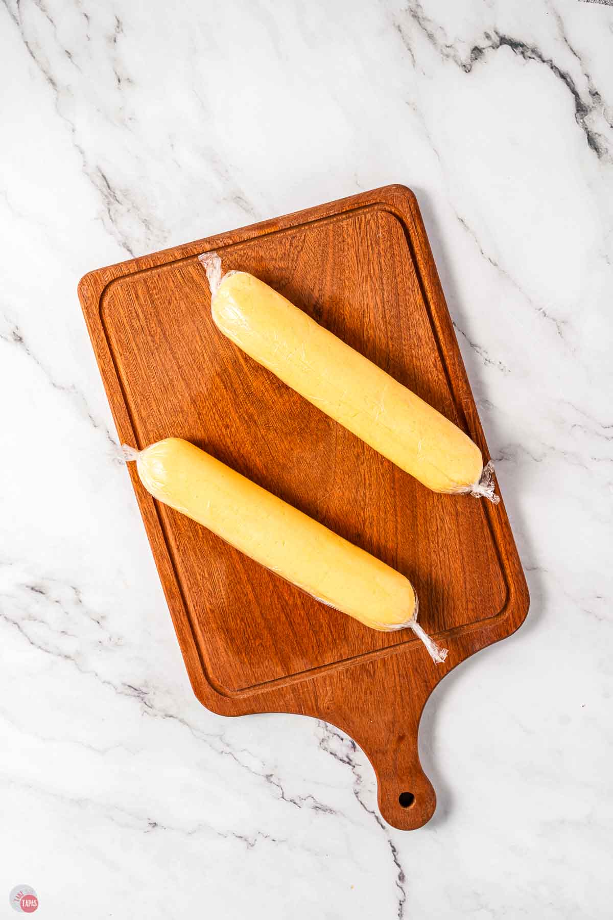 two logs of cookie dough on a cutting board