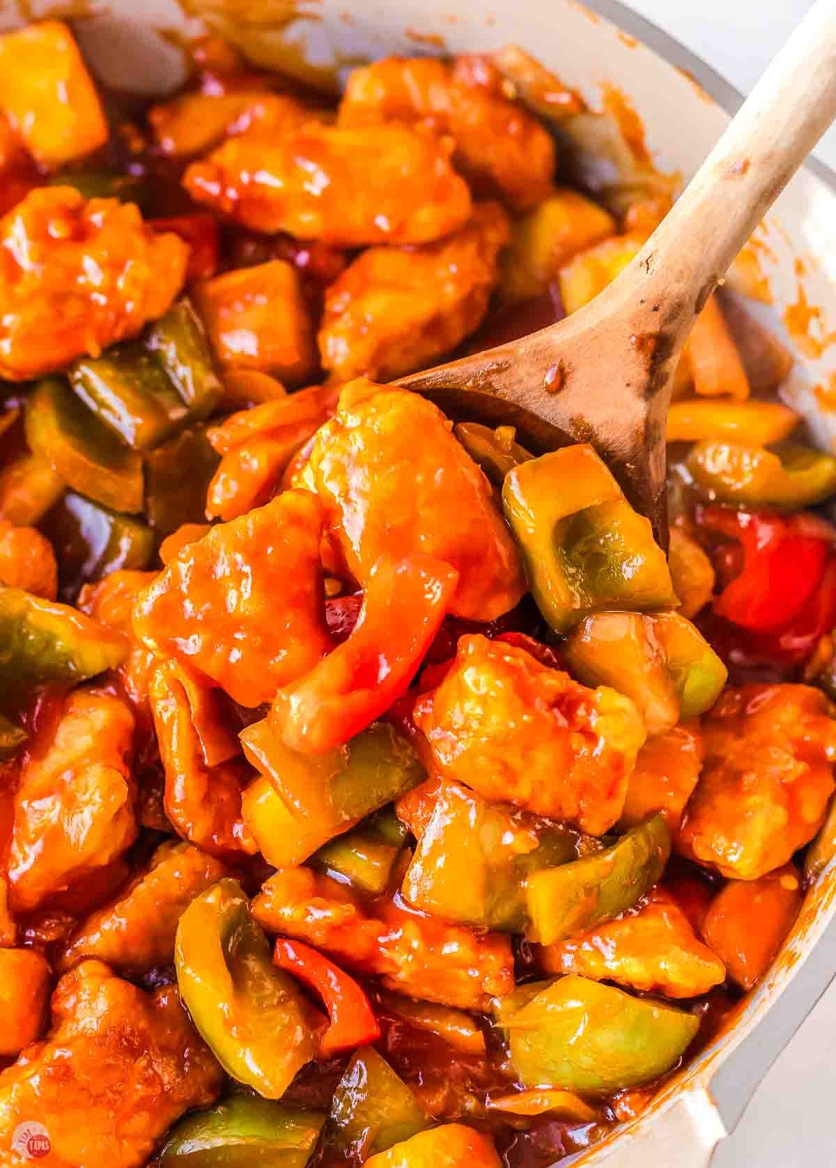 wood spoon scooping chicken with bell peppers out of a skillet