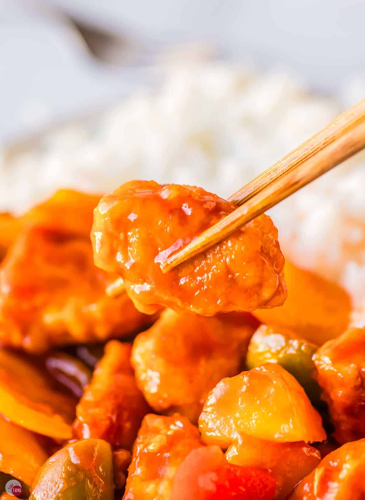 chopsticks holding piece of sweet and sour chicken