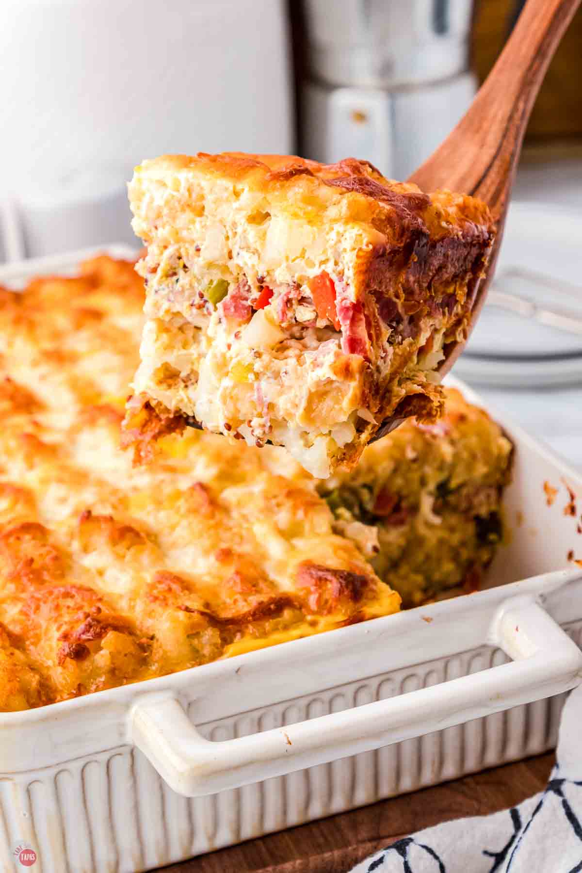 scoop of corned beef casserole on a wood spoon above a large dish