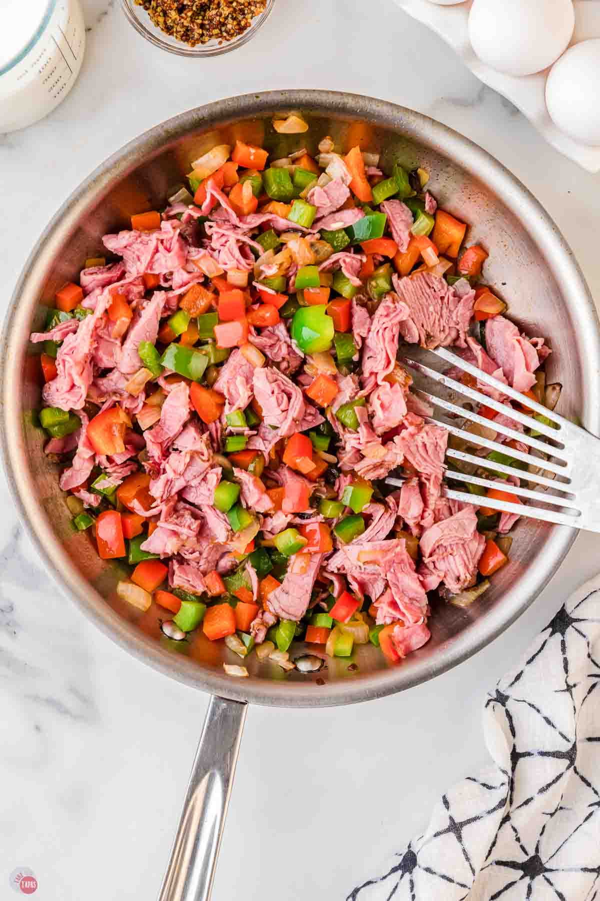 corned beef and vegetables being cooked in a silver skillet with a metal spatula