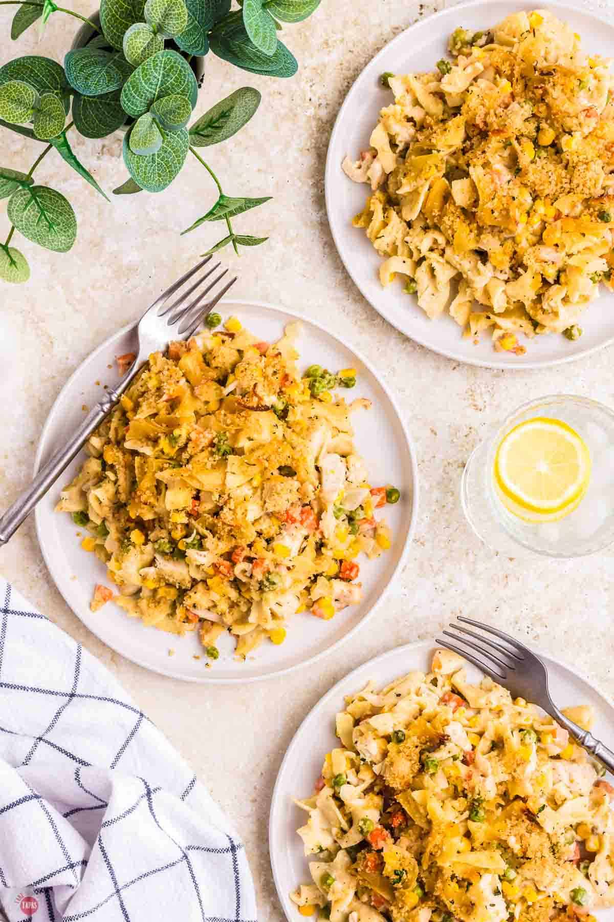 three plates of chicken casserole with forks and a glass of lemon water