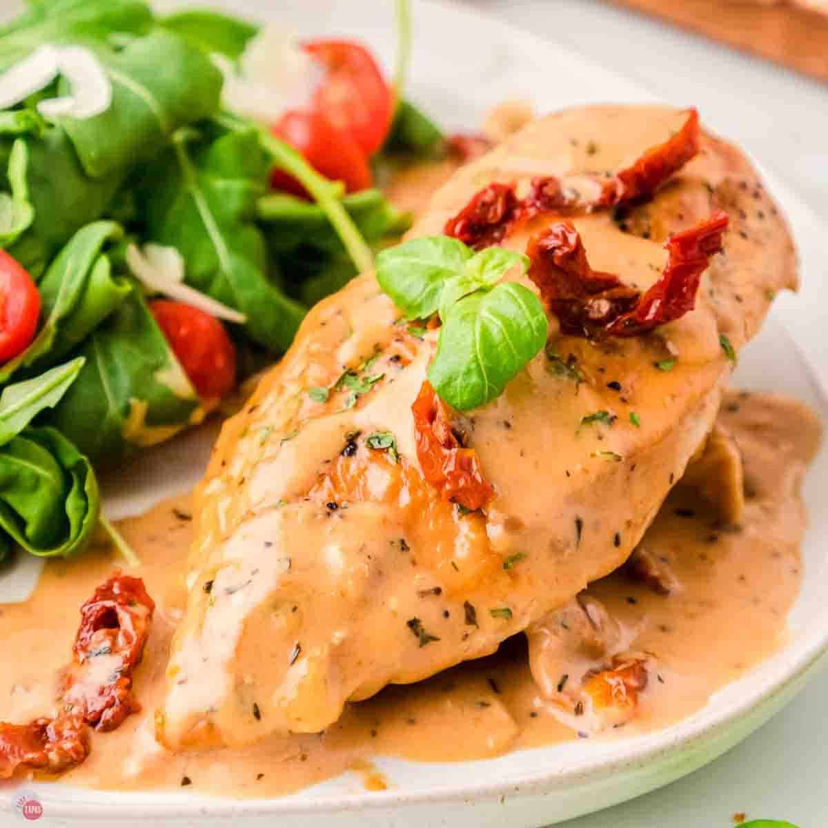 chicken breast covered in sauce on a plate next to a salad