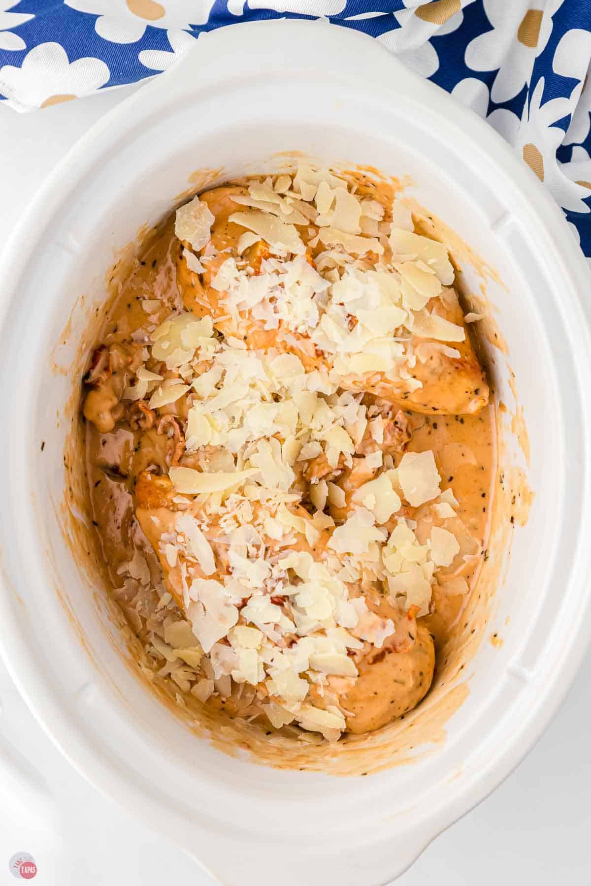 white slow cooker with chicken, cream sauce, and shave parmesan cheese on top