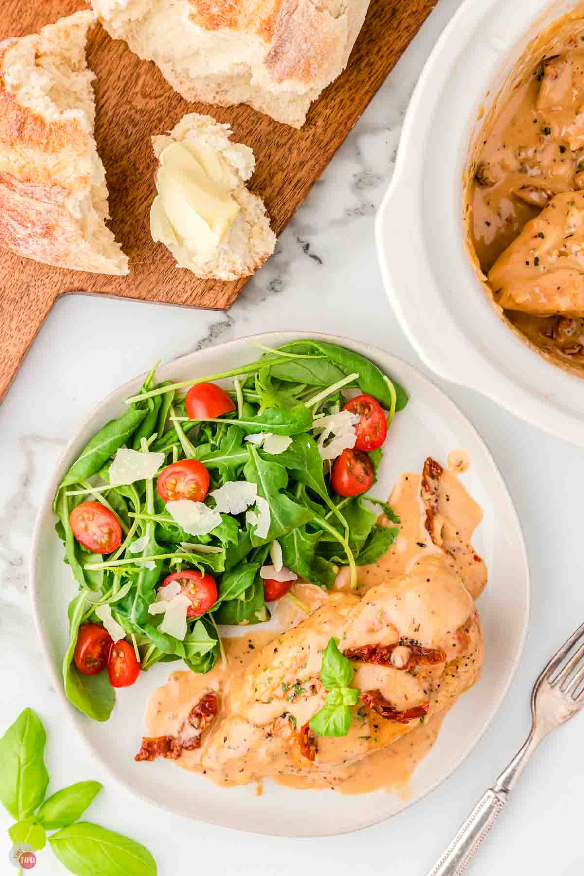 plate of chicken and salad next to a board with bread on it