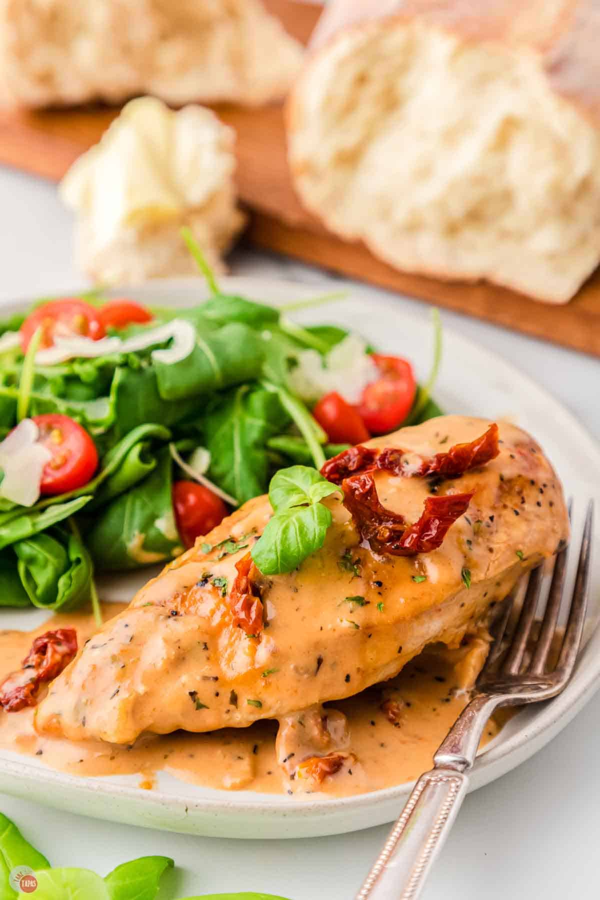 plate of Marry me chicken with bread and a crockpot in the back