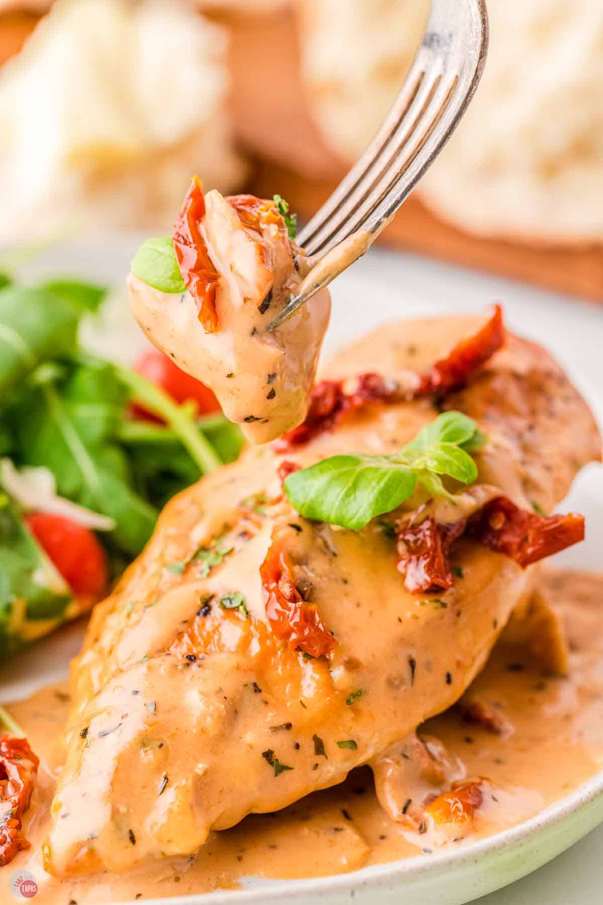 fork with a bite of chicken on it over a plate with a salad