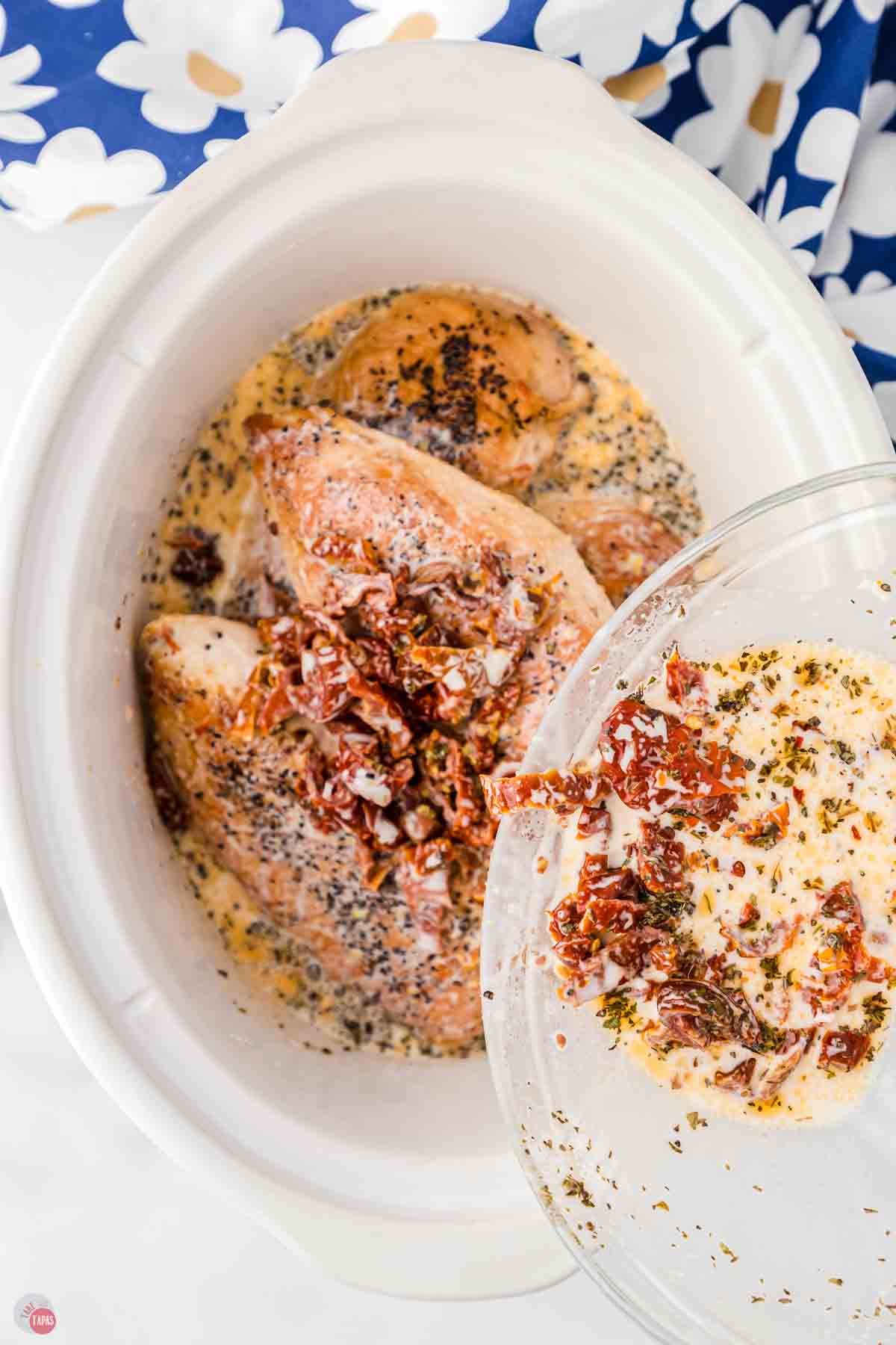 white crockpot with chicken and a bowl of sauce being poured in