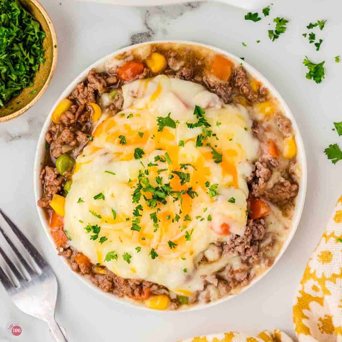 bowl of crockpot shepherds pie with a fork and bowl of parsley next to it