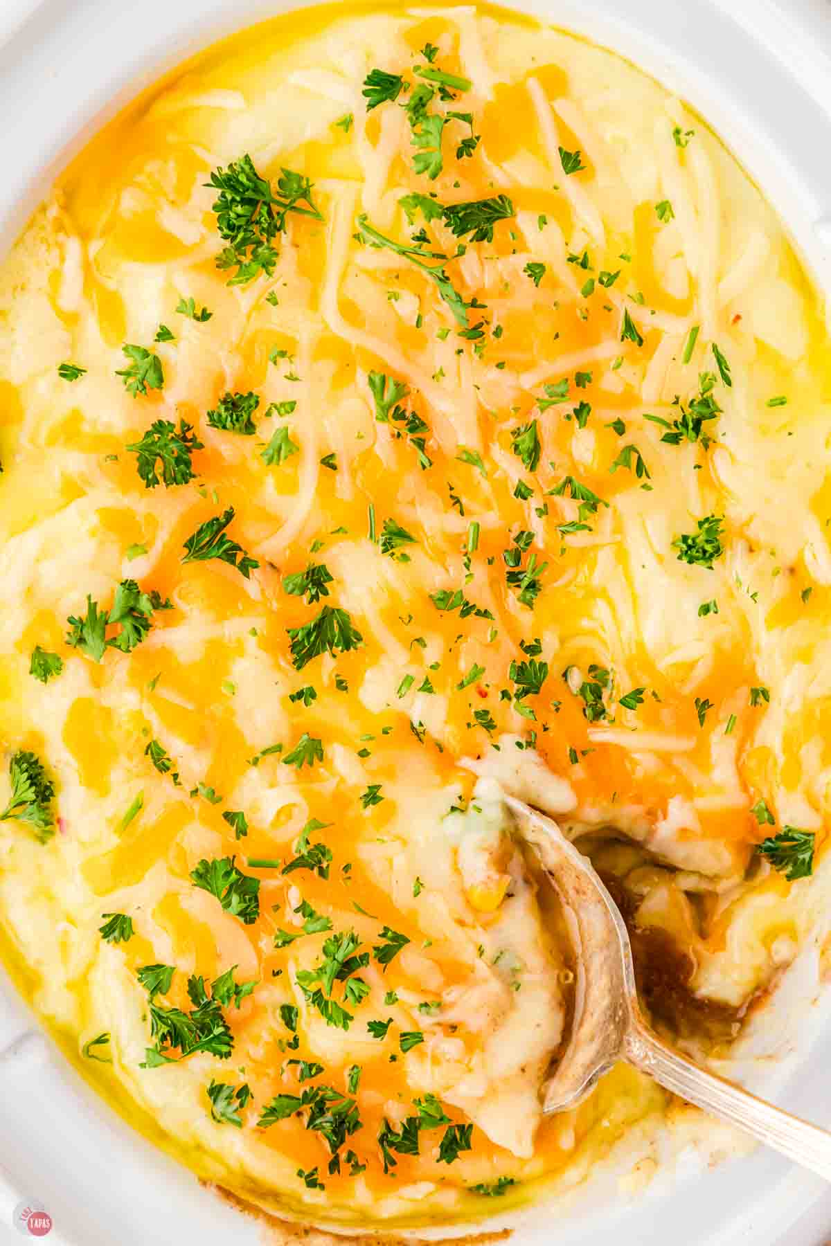 mashed potatoes topped with cheese and parsley with a spoon taking a scoop out