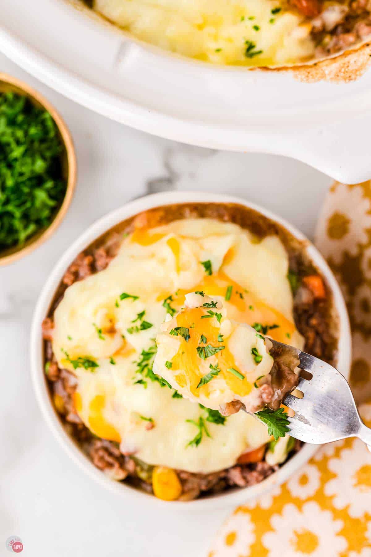 bowl of mashed potatoes and ground beef with a fork taking some cheese off the top
