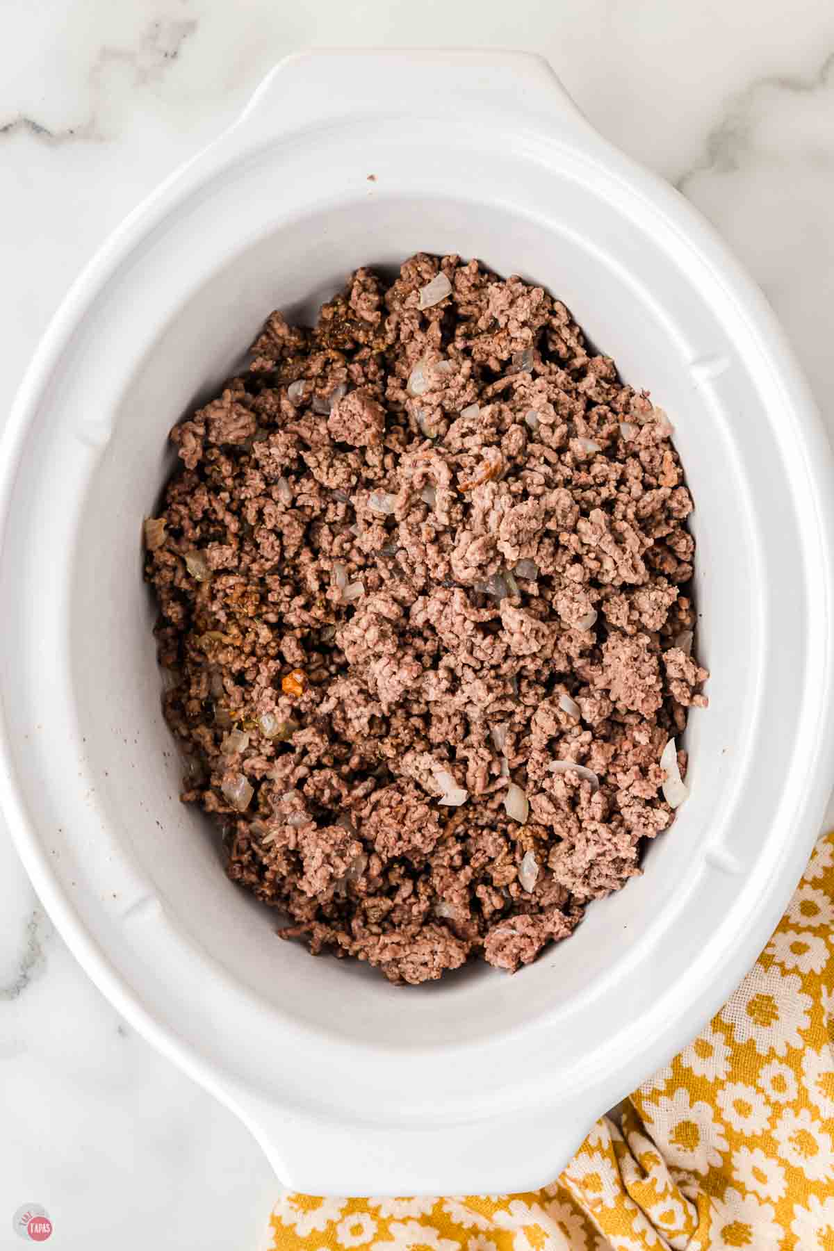cooked ground beef in a white slow cooker pot