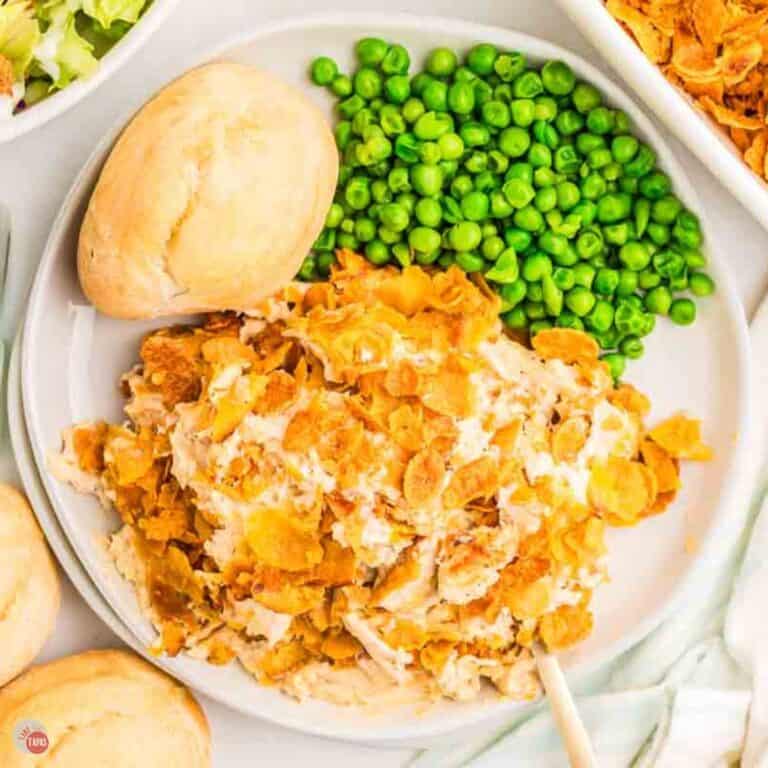white plate with chicken, peas, and a dinner roll on it