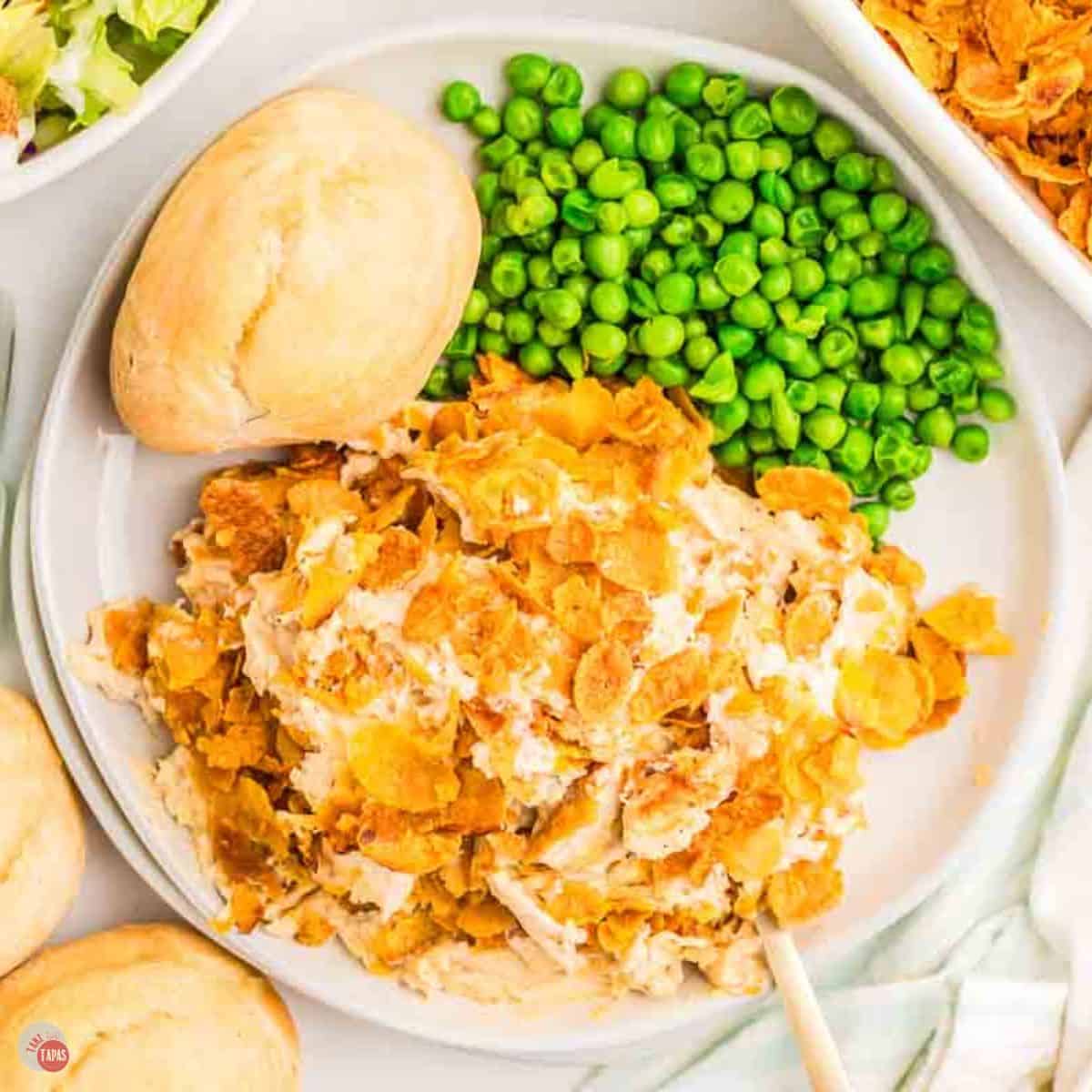 white plate with chicken, peas, and a dinner roll on it