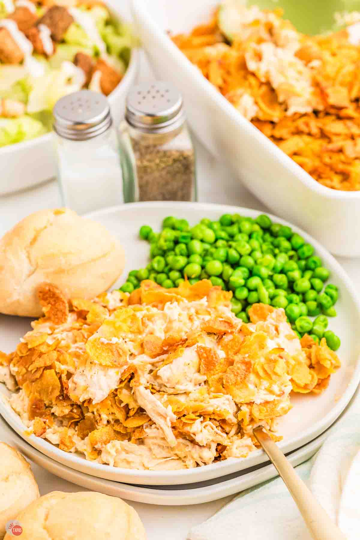 plate of casserole with green peas and a dinner roll