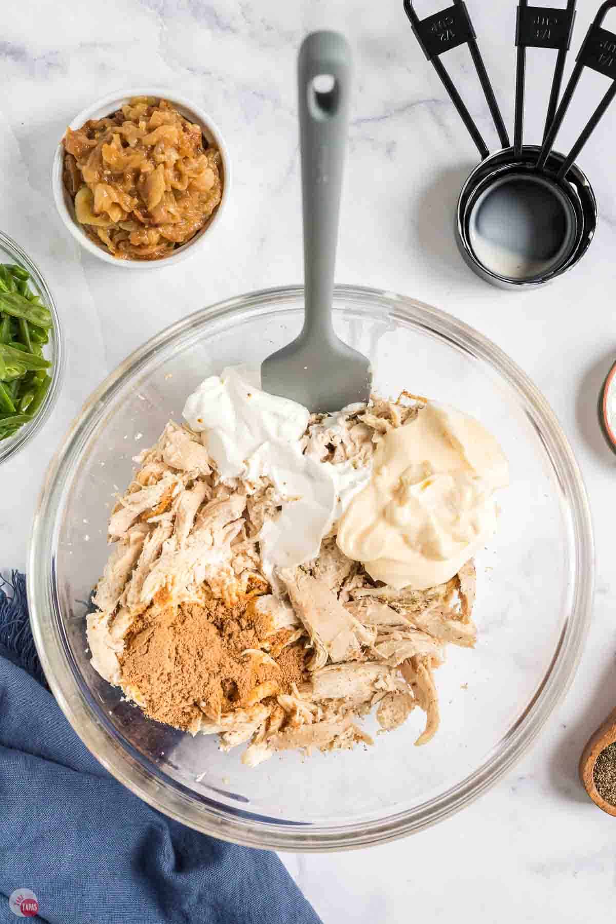 clear bowl with chicken, mayo, and spices in it with a grey spatula