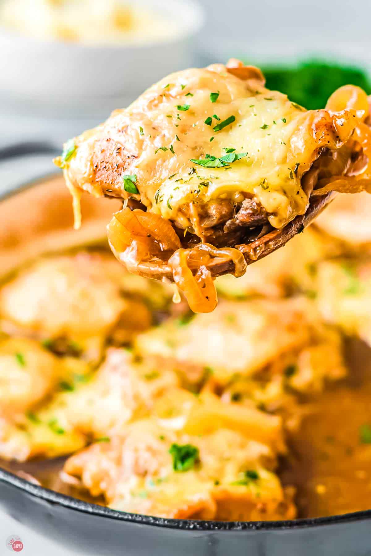 wood spoon holding a chicken thigh topped with melted cheese