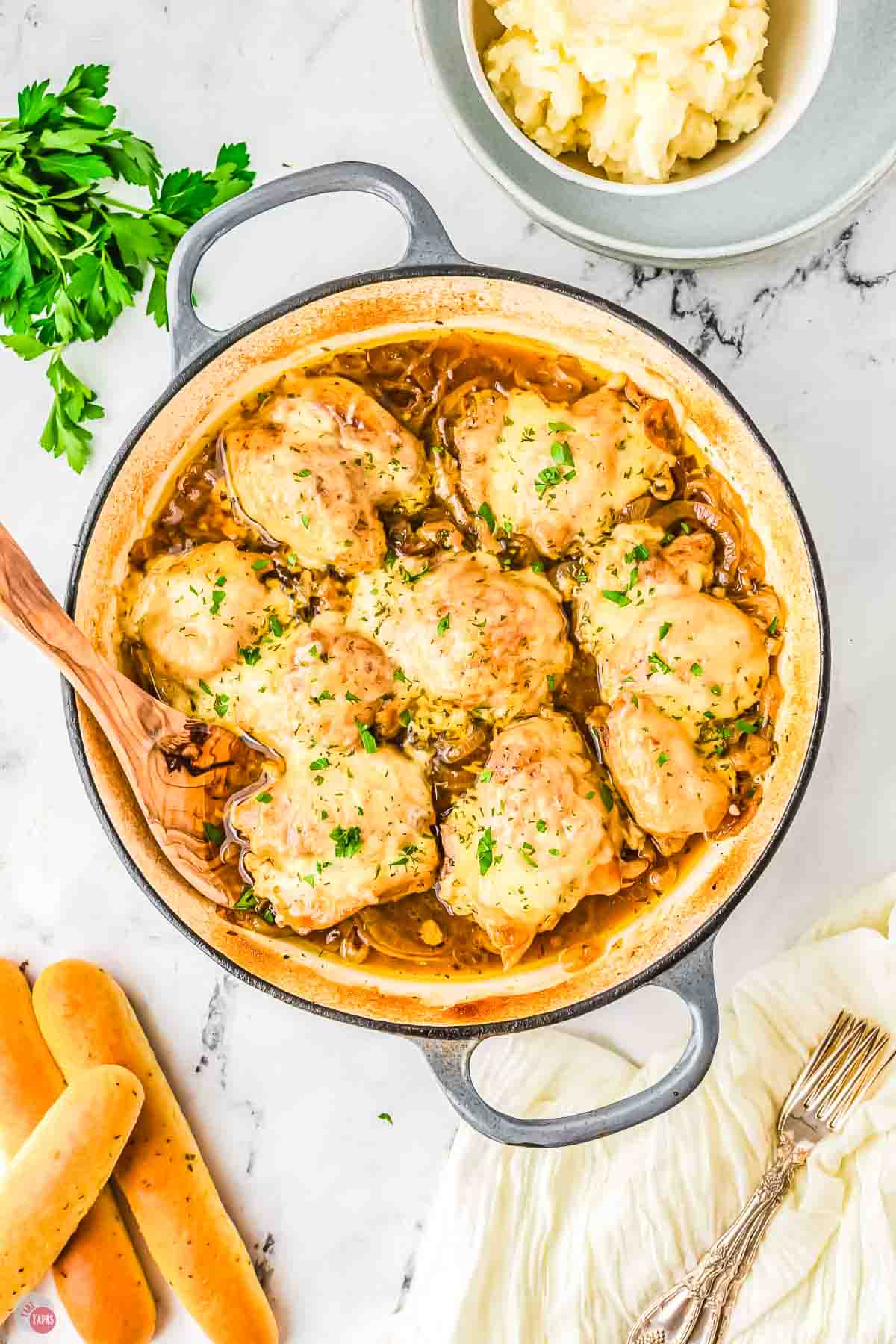 white skillet with chicken thighs and melted cheese on top with a wood spoon in it