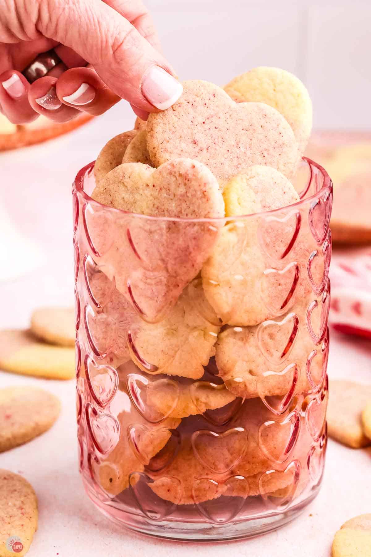 hand picking a cookie out of a clear, pink jar