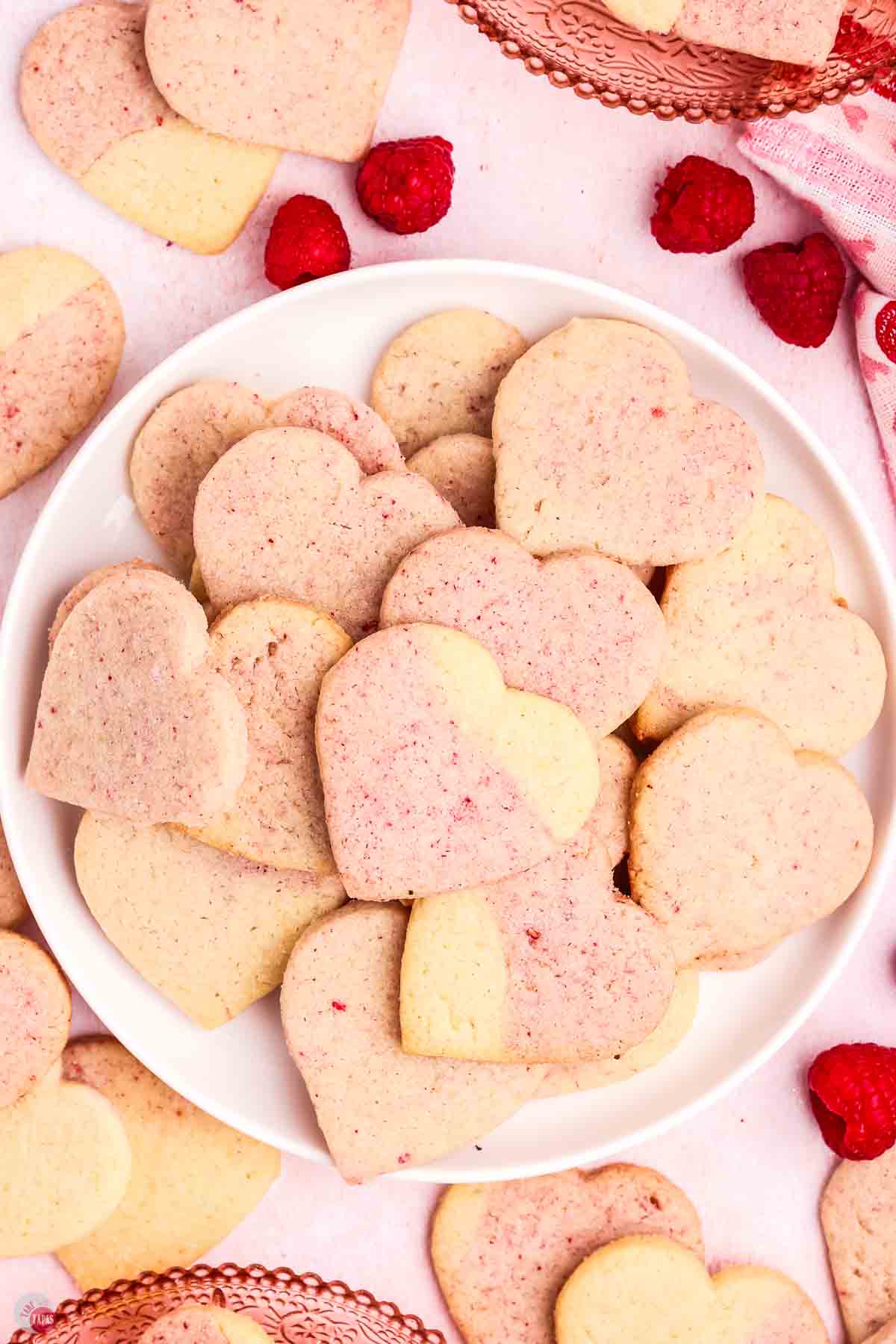 heart shaped sugar cookies on a white plate with raspberries next to it