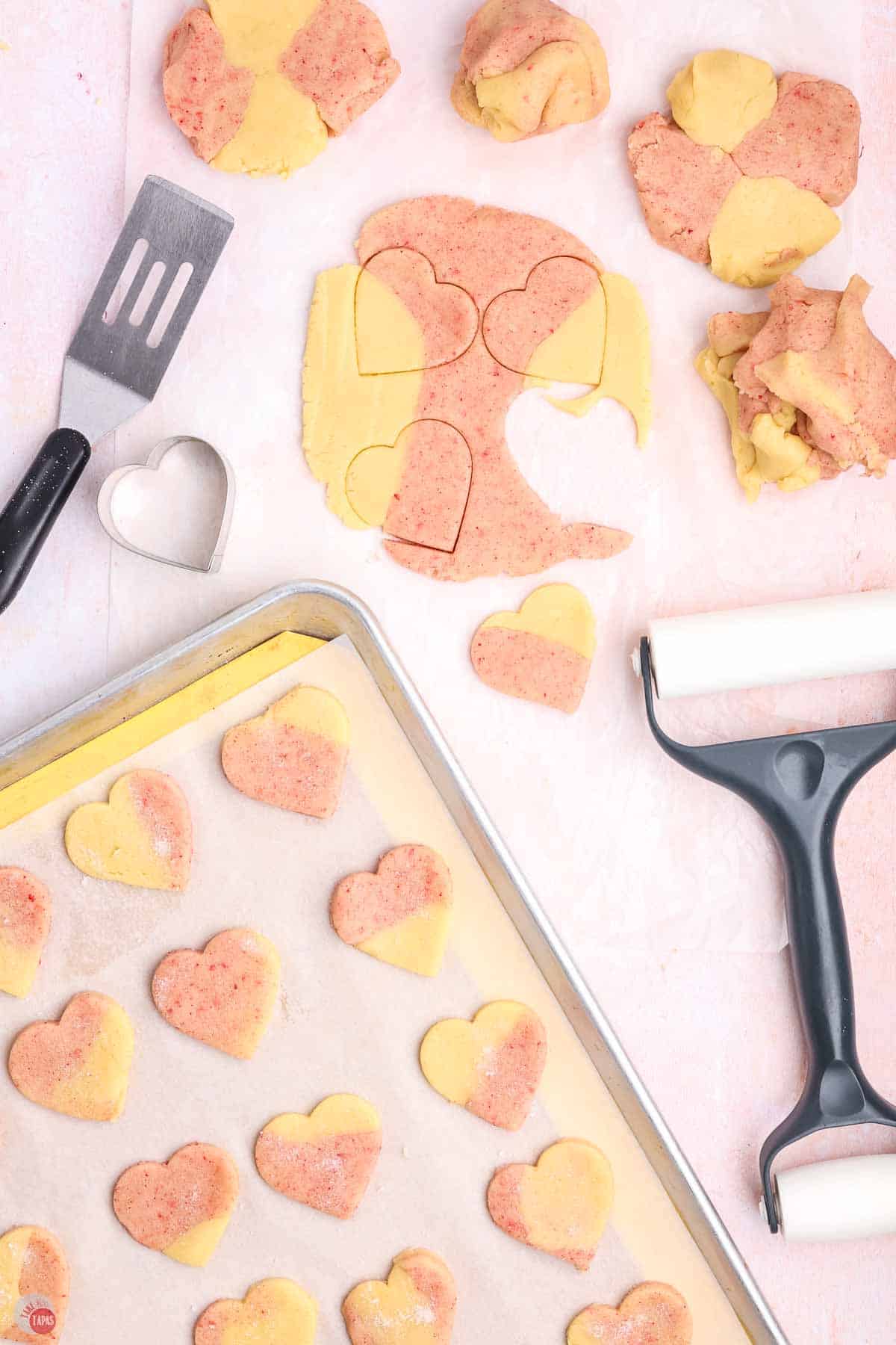 pink and yellow cookie dough being cut into heart shapes