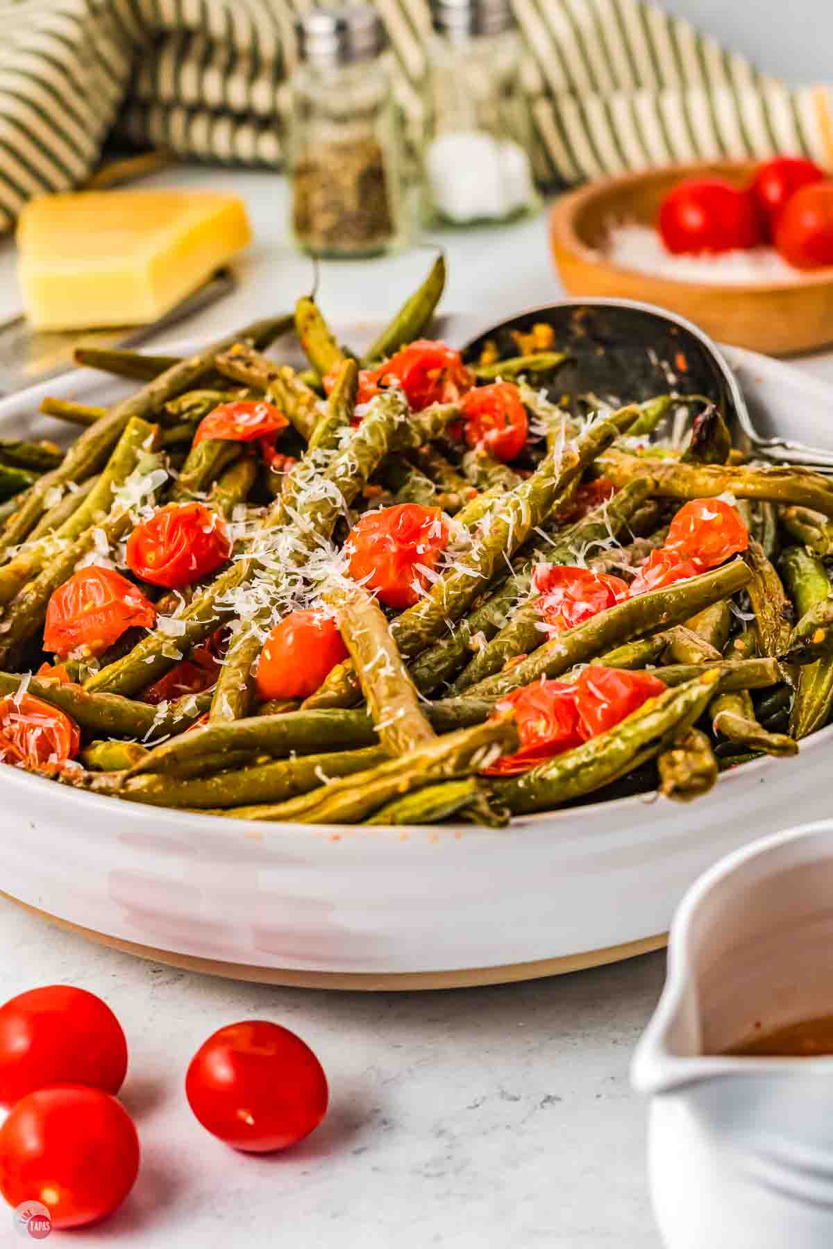 green beans and tomatoes in a large white bowl and topped with shredded cheese