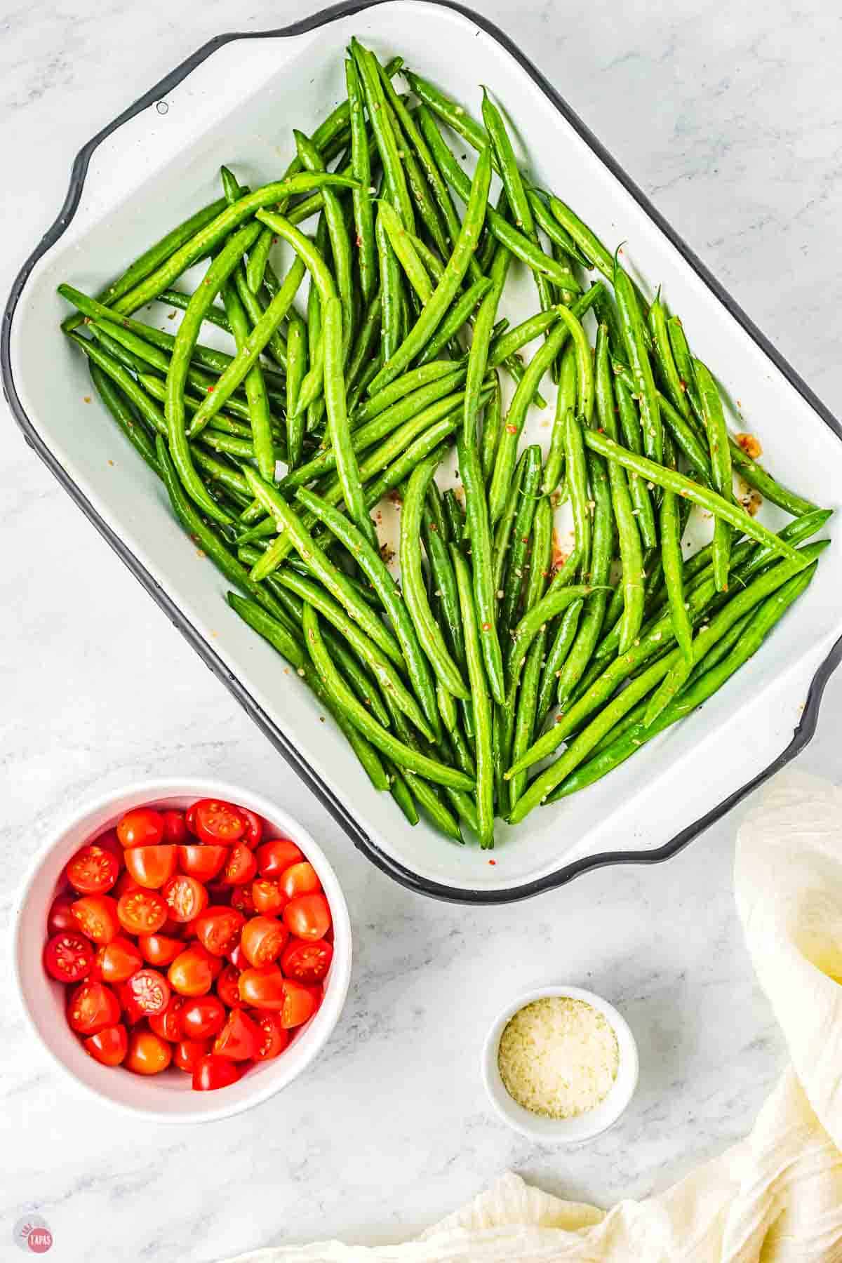 green beans in a baking dish next to a bowl of cut tomatoes