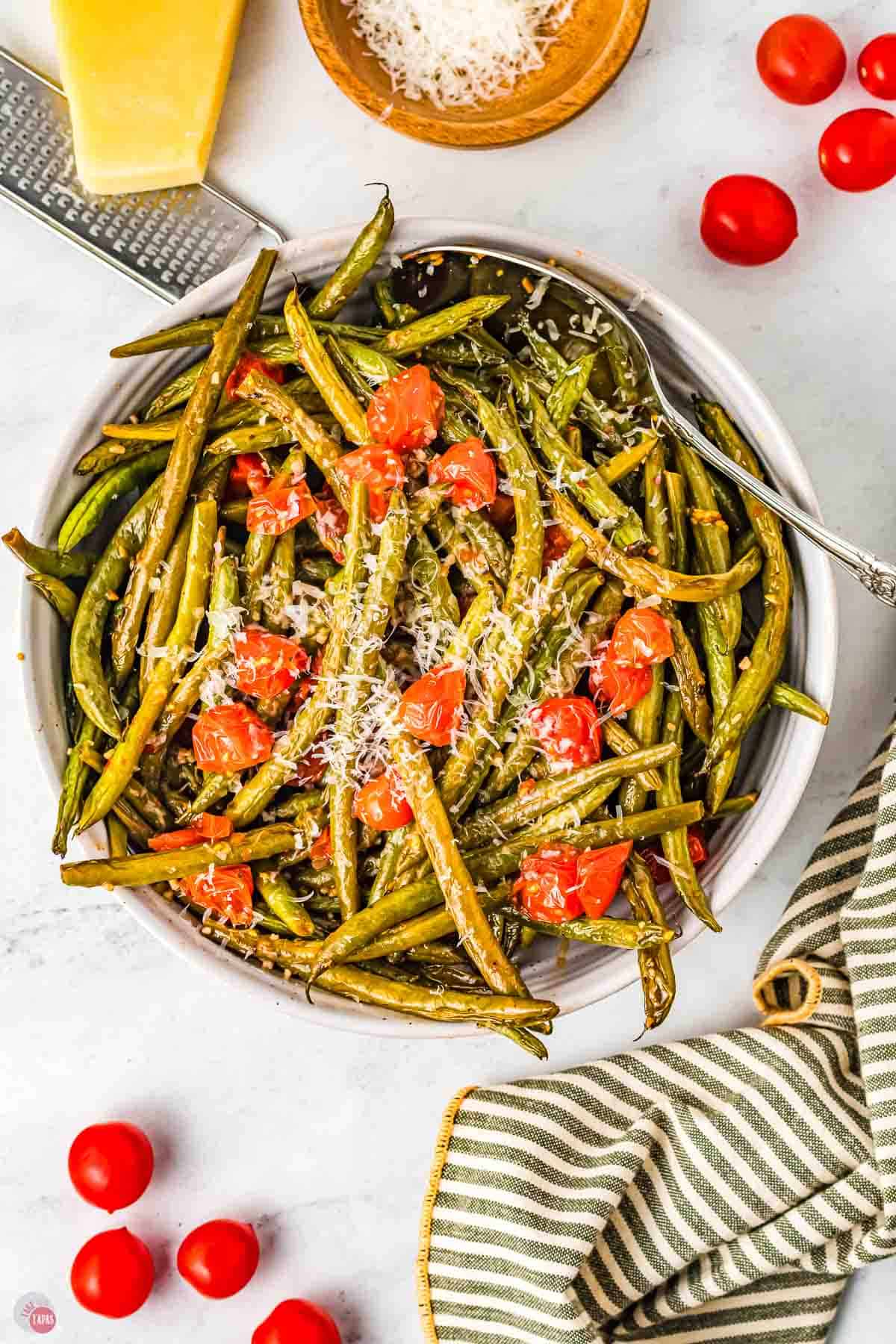 bowl of green beans and tomatoes next to a striped napkin