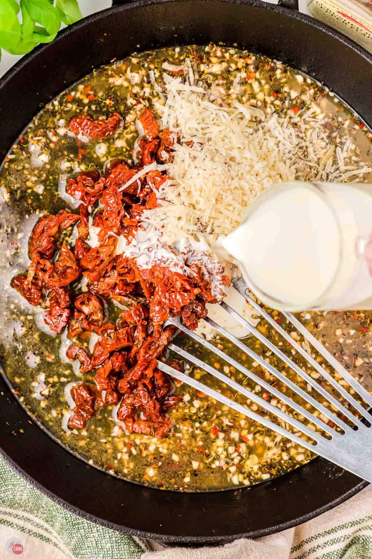 spatula stirring broth, sun-dried tomatoes, and cheese in a skillet