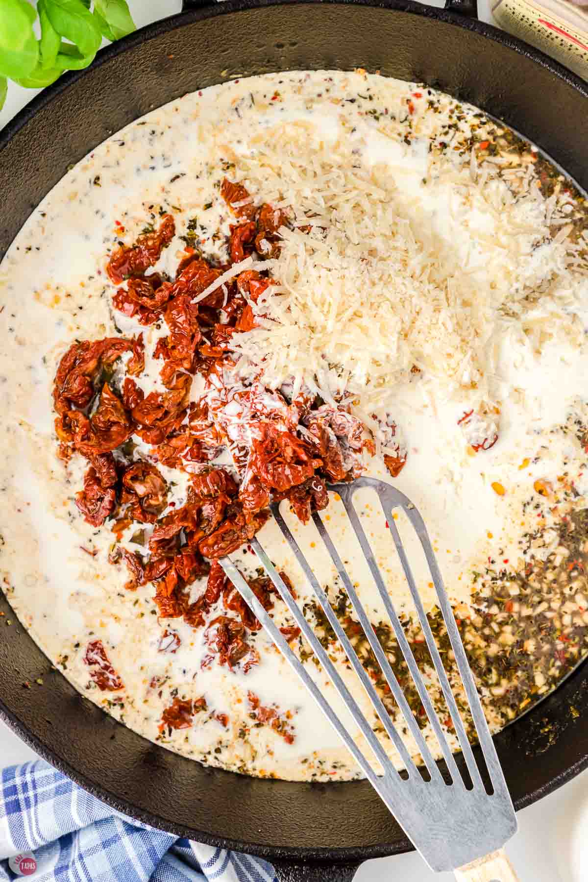 skillet with a spatula stirring in cream and sun-dried tomatoes