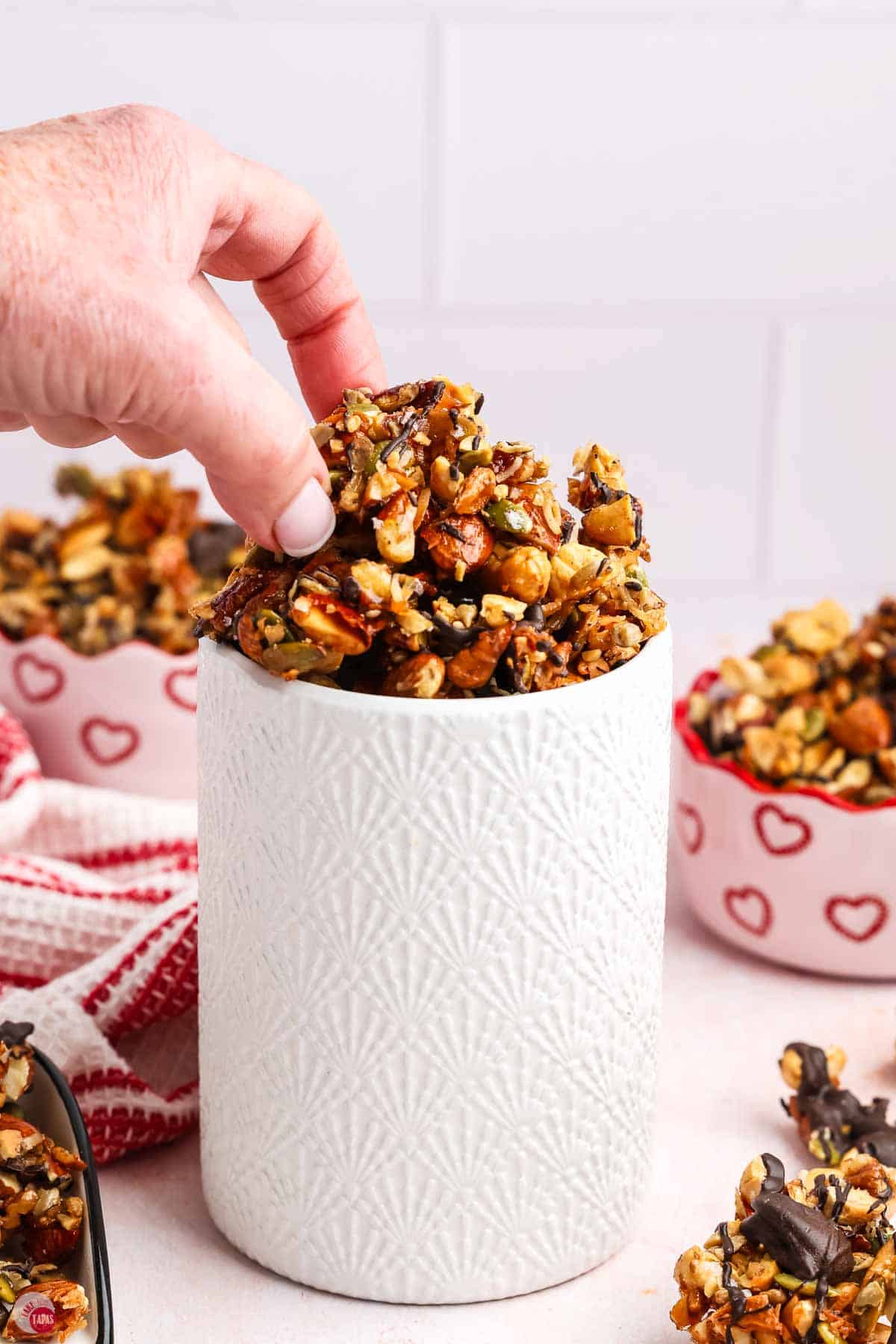 hand grabbing a nut and seed cluster out of a white jar