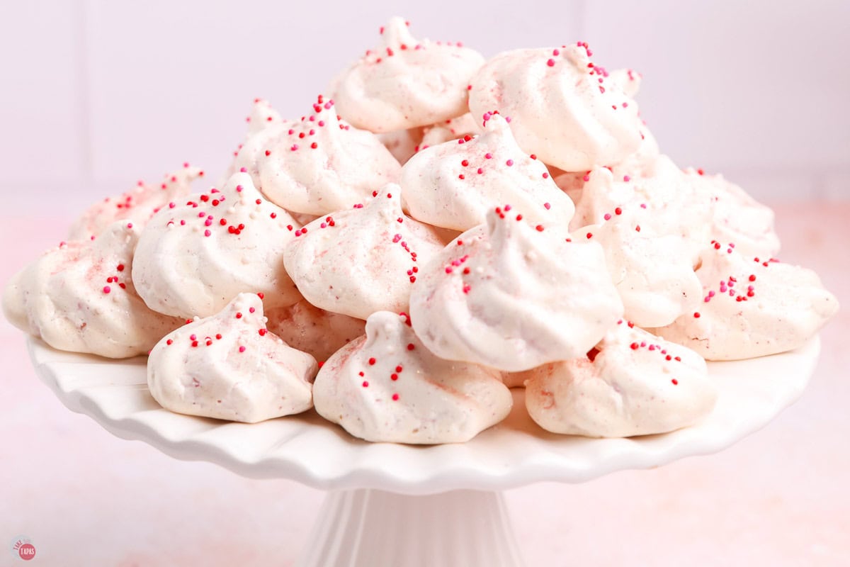 white cake plate with pink meringue cookies in a stack on top of it