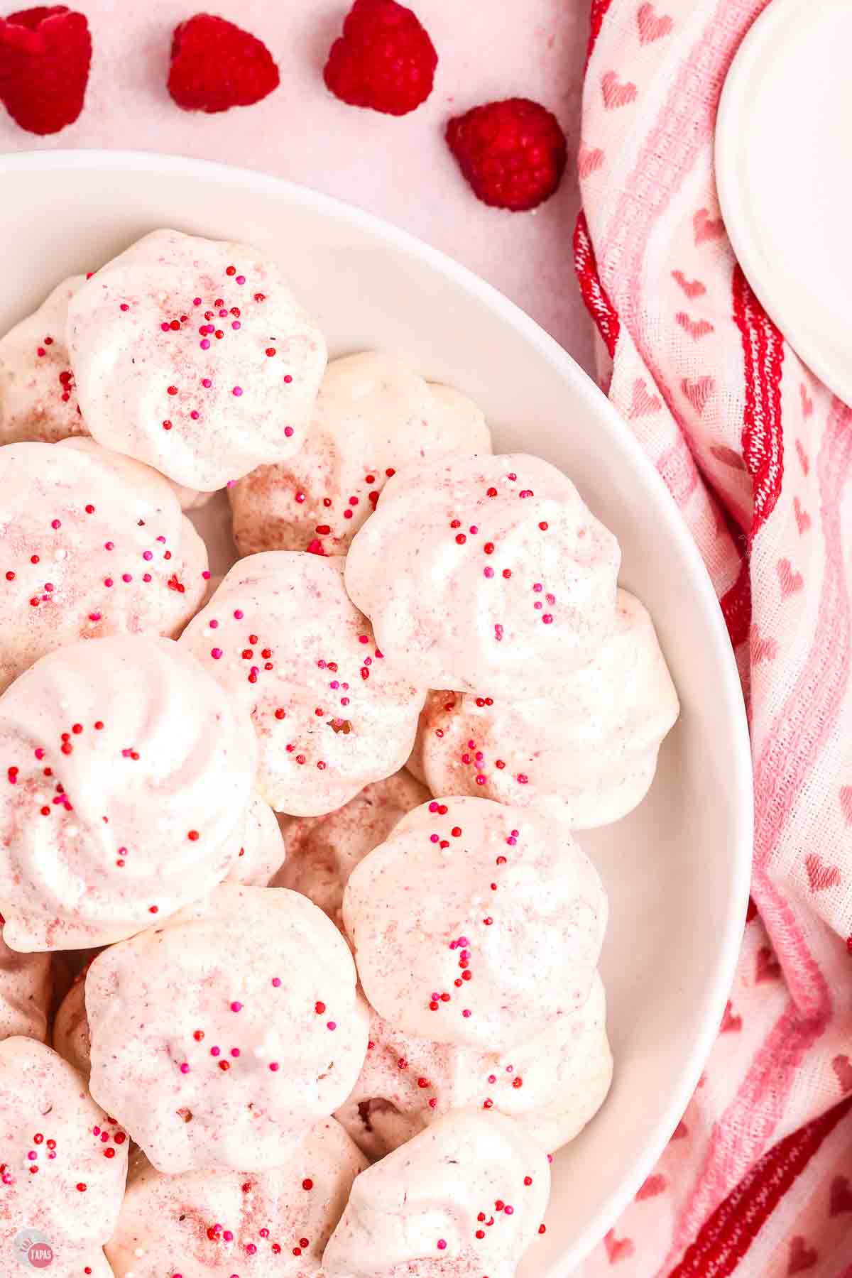close up of raspberry meringue cookies in a bowl with a heart napkin next to it