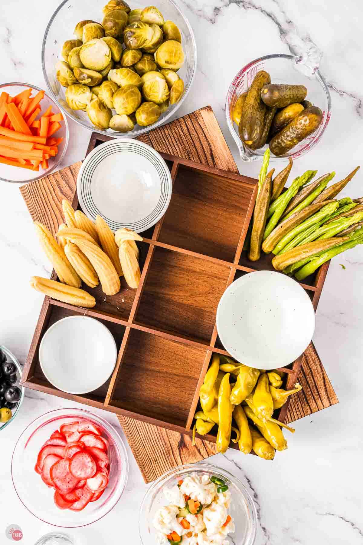 Assorted pickles in a wood tray with white bowls